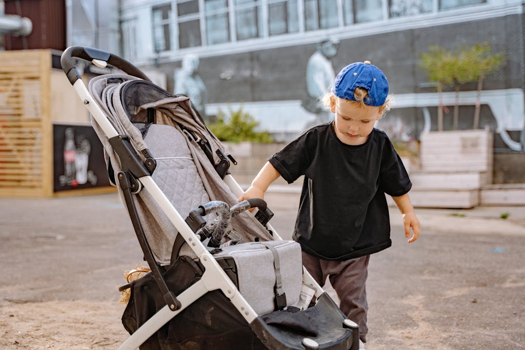 A young child in casual wear examines a stroller on a vibrant urban street.