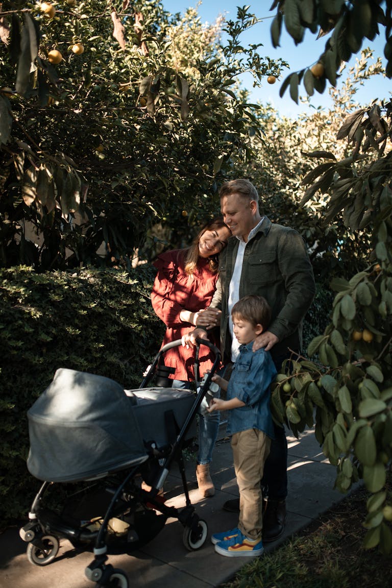 Family enjoying a sunny walk in the park, pushing a stroller, surrounded by greenery.